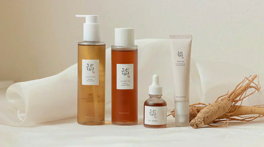 Koreansk hudplejerutine stillet op i rækkefølge: rensolie, toner, serum og creme på lyst underlag