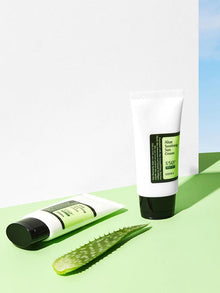 COSRX Aloe Soothing Sun Cream SPF50 solcreme med aloevera. 2 tuber på et grøn bord