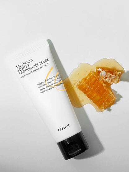 COSRX Full Fit Propolis Honey Overnight Mask på et bord med honning ved siden af 